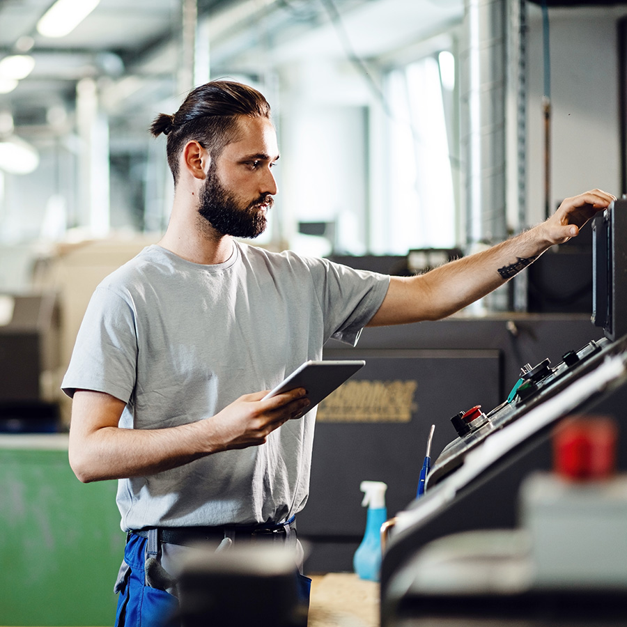 Industrial engineer using touchpad while operating a CNC machine in a factory.